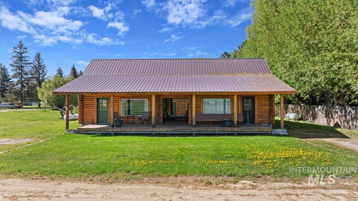 View of front facade with covered porch, a front yard, log exterior, and a metal roof