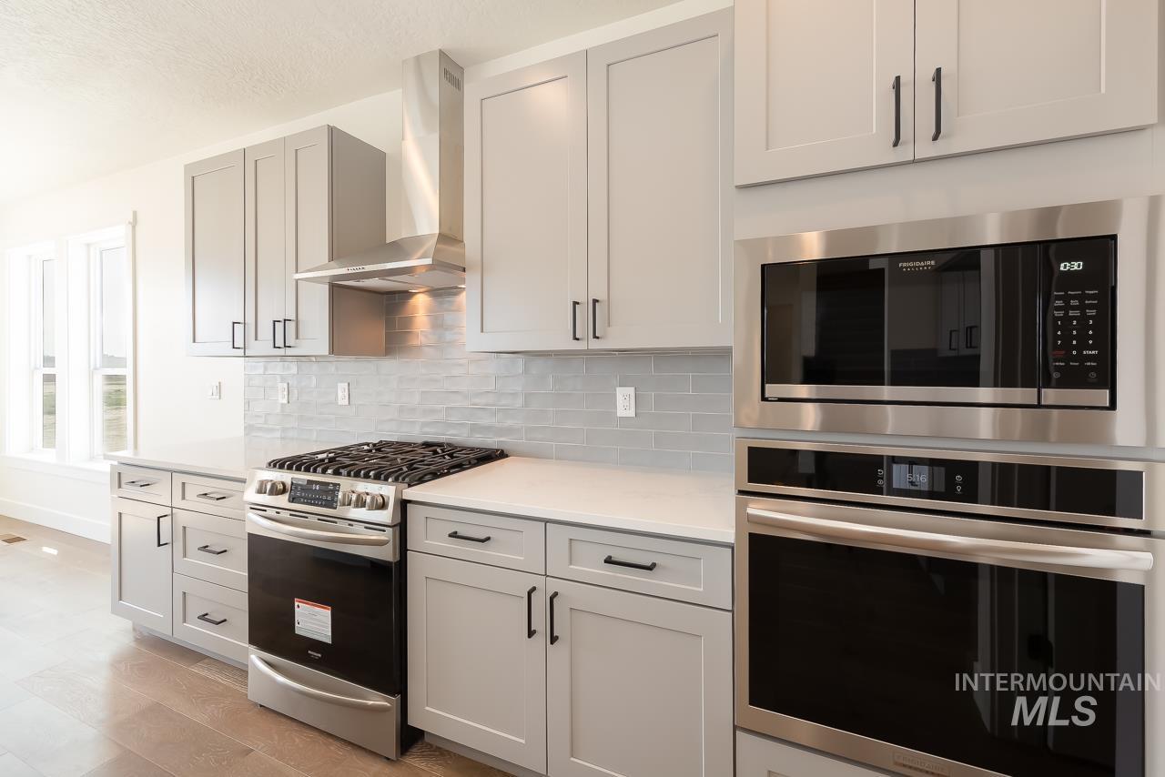 Kitchen featuring appliances with stainless steel finishes, wall chimney exhaust hood, backsplash, light wood-style floors, and light stone countertops
