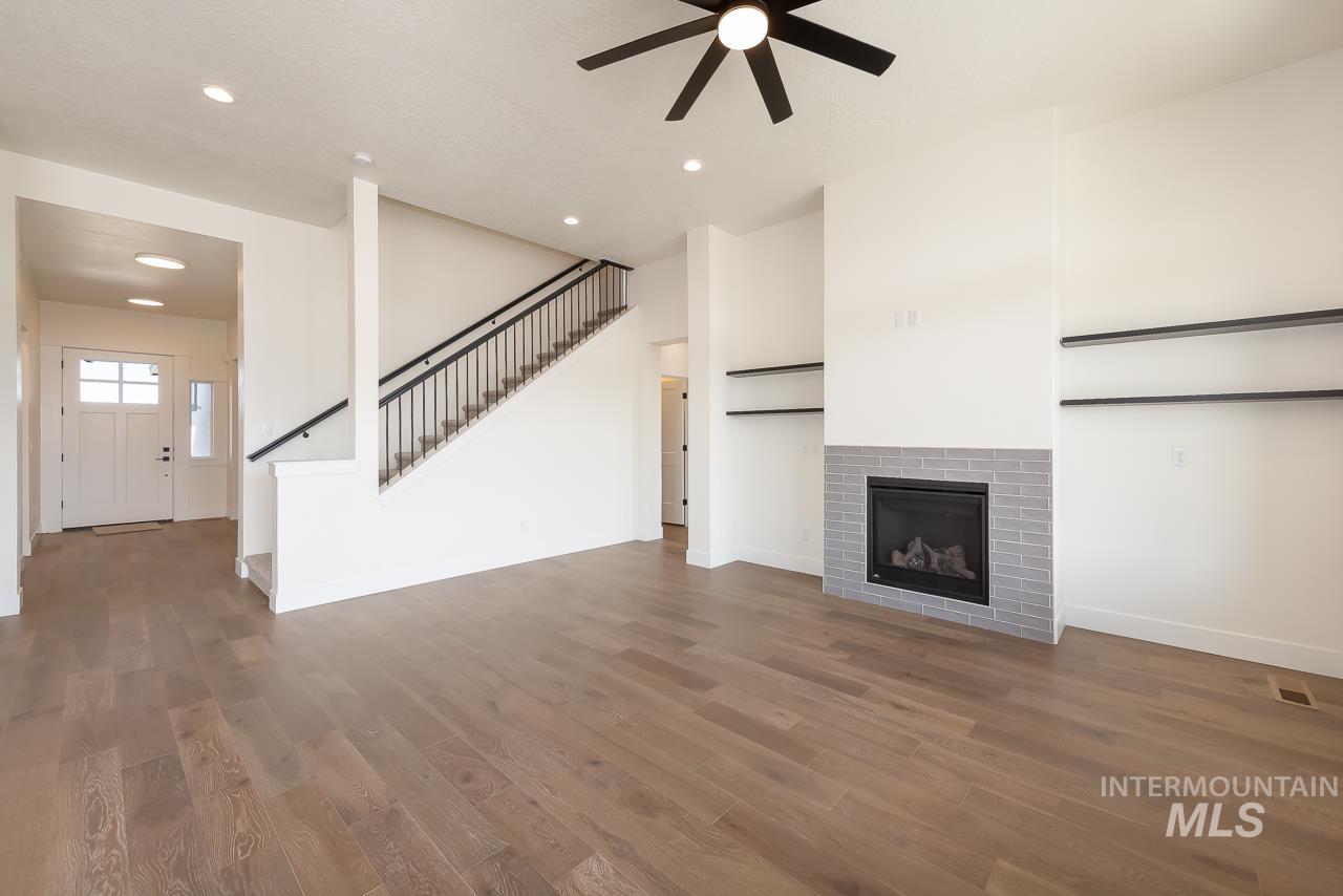 Unfurnished living room featuring recessed lighting, a brick fireplace, wood finished floors, stairs, and ceiling fan