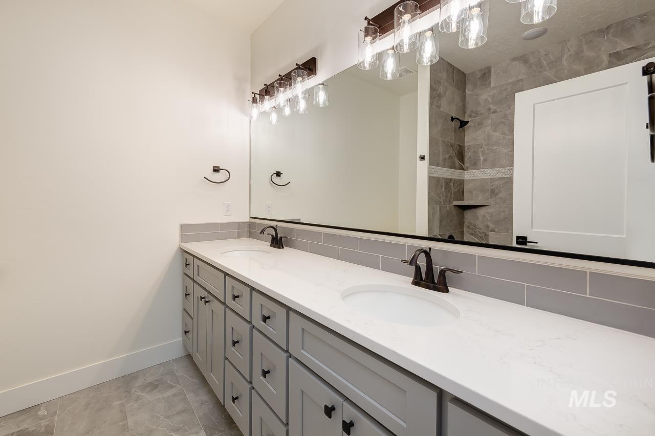 Full bath featuring double vanity, tasteful backsplash, and tiled shower