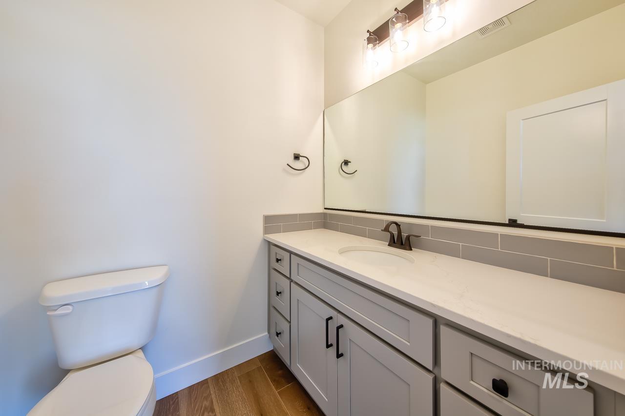 Half bath with vanity, dark wood-style flooring, and tasteful backsplash