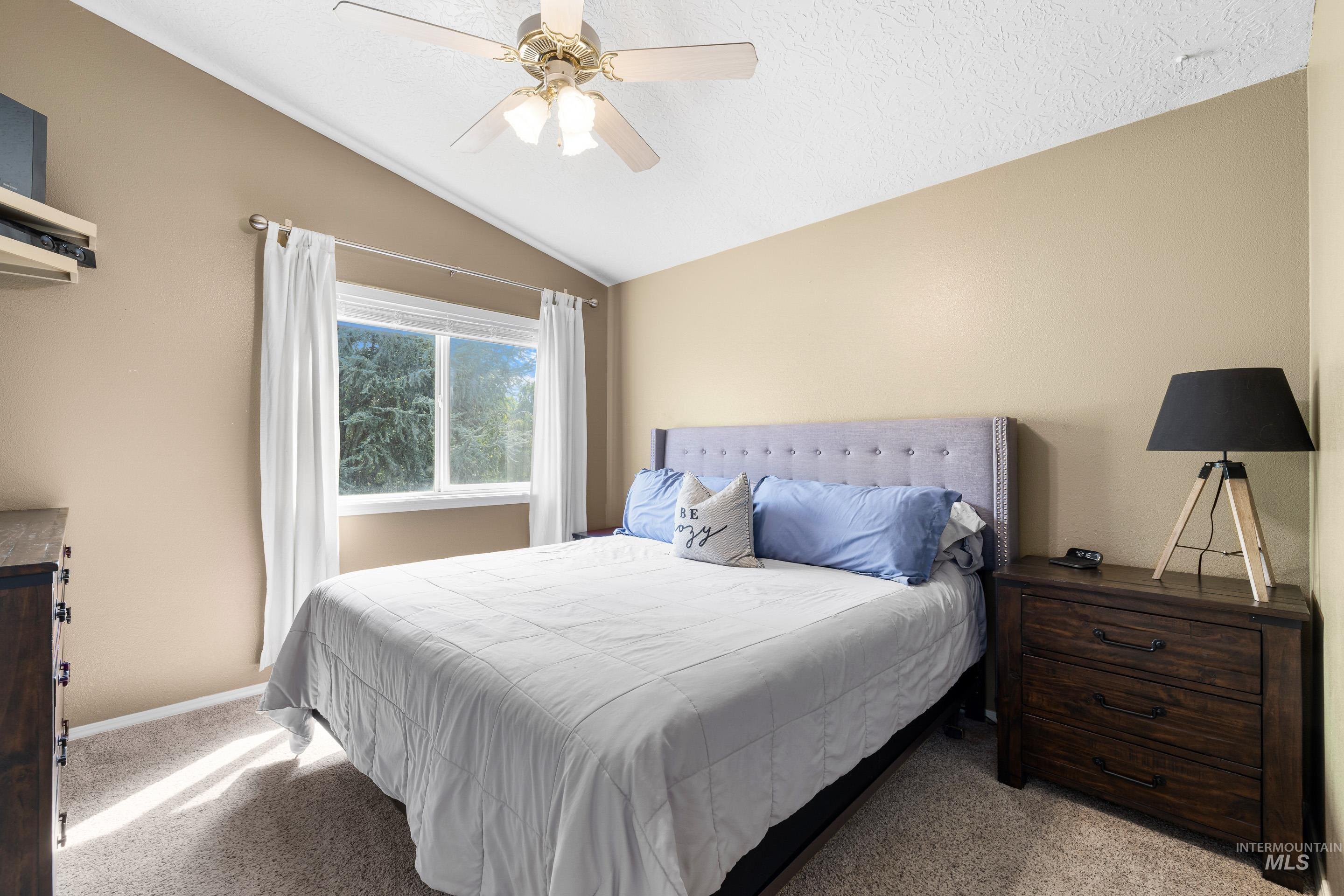 Bedroom featuring carpet, vaulted ceiling, a ceiling fan, and a textured ceiling