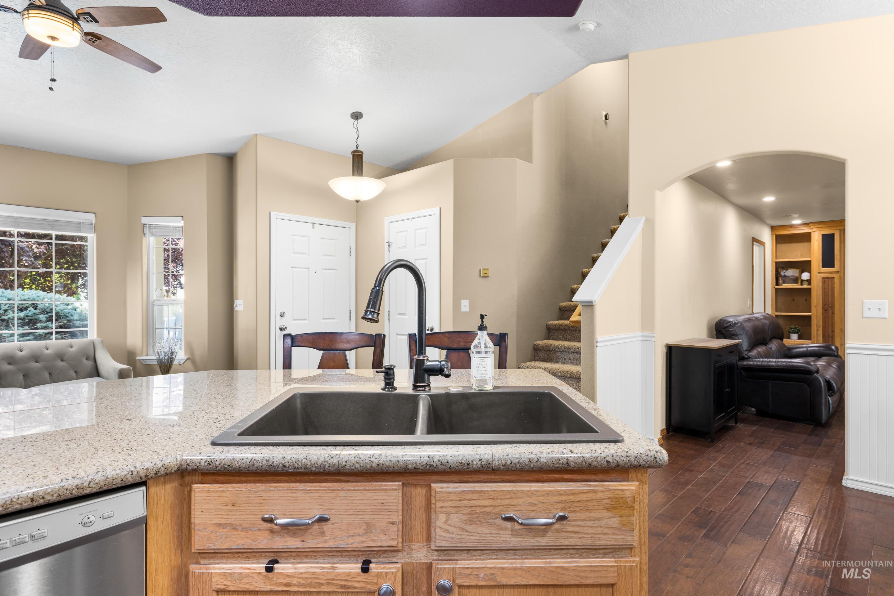 Kitchen with open floor plan, stainless steel dishwasher, dark wood-type flooring, hanging light fixtures, and arched walkways