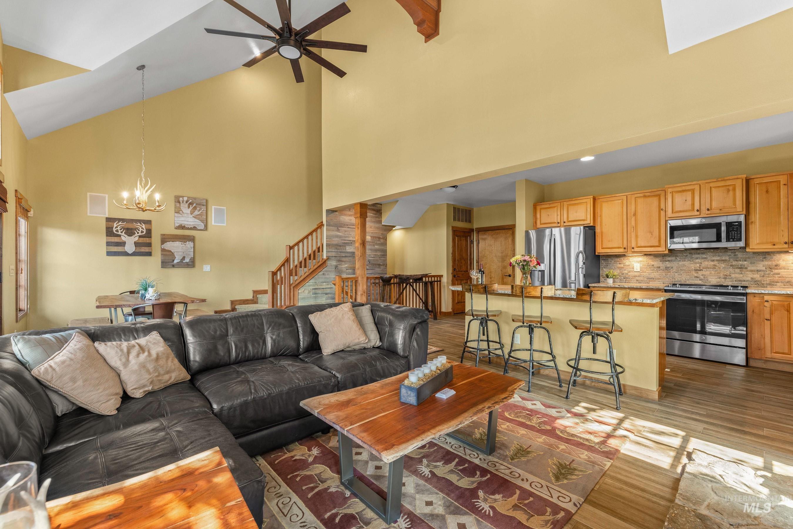 Living area with newly finished floors, ceiling fan, a chandelier, high vaulted ceiling, and stairway