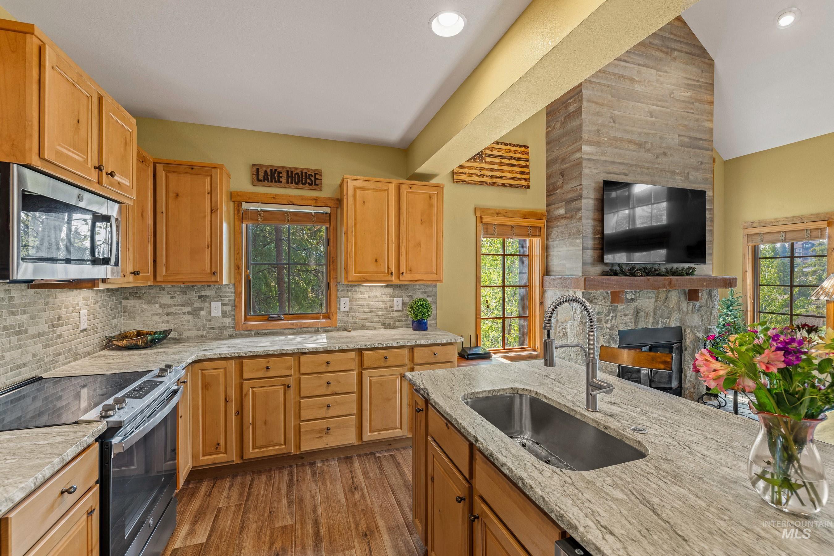 Kitchen featuring stainless steel appliances, newly finished floors, new granite countertops, tasteful backsplash, and a large fireplace