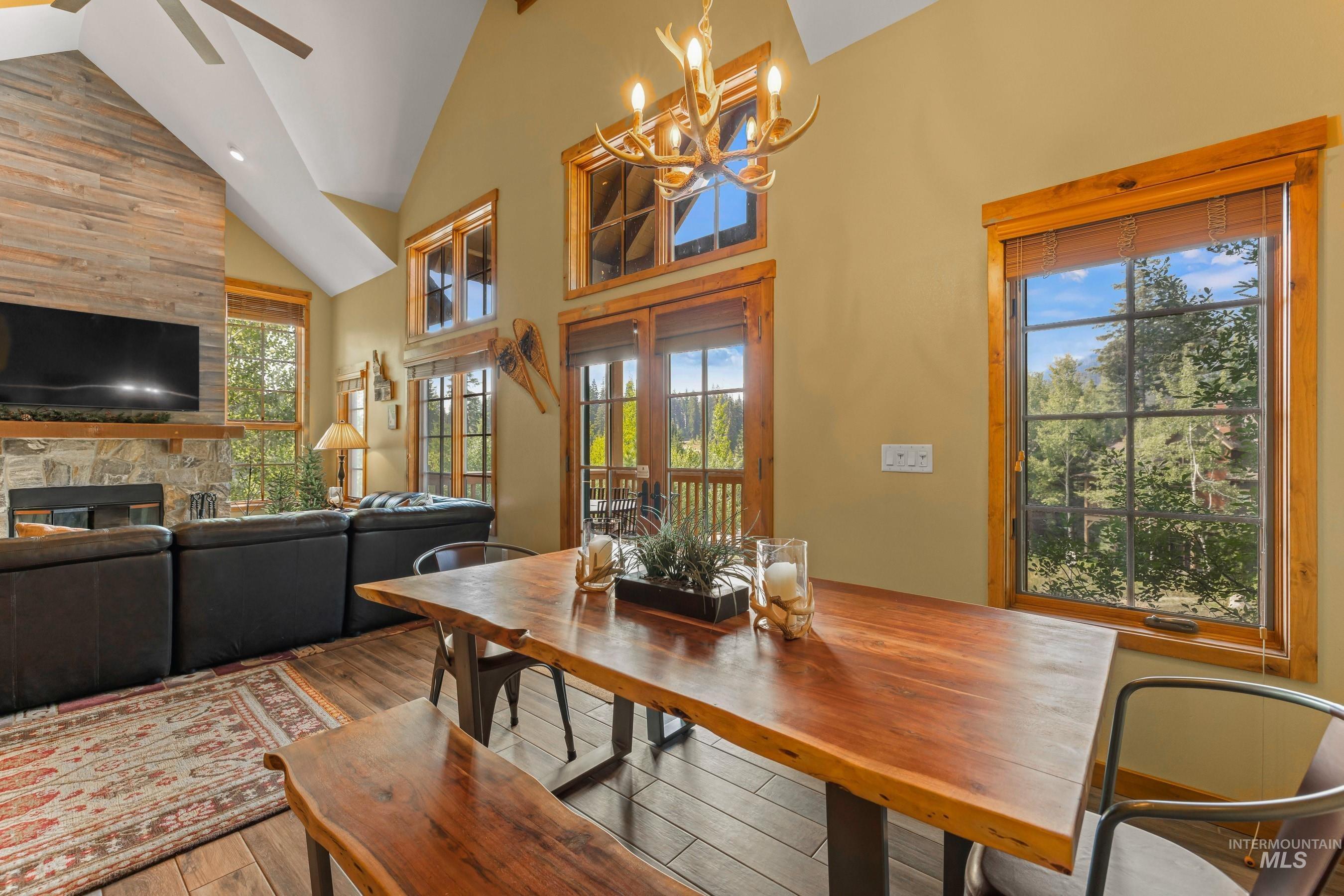 Dining space featuring high vaulted ceiling, newly finished tile flooring, a stone fireplace, a chandelier, and a ceiling fan