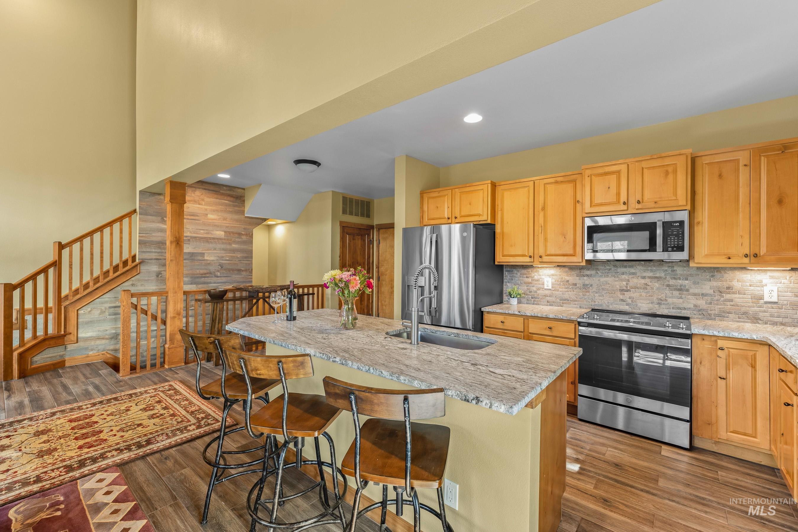 Kitchen with appliances with stainless steel finishes, new tile floors, new granite counters, backsplash, and a center island with sink and dishwasher