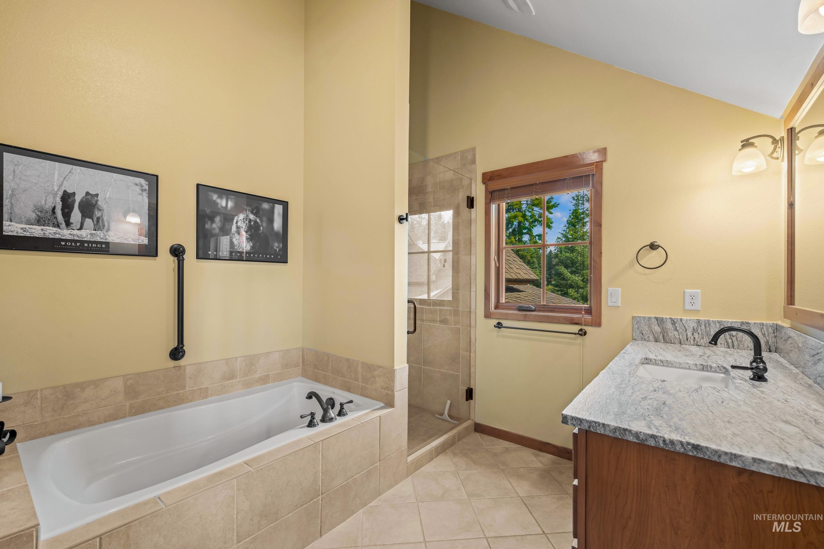 Primary bathroom with a stall shower, bathtub, new vanity countertop, and lofted ceiling