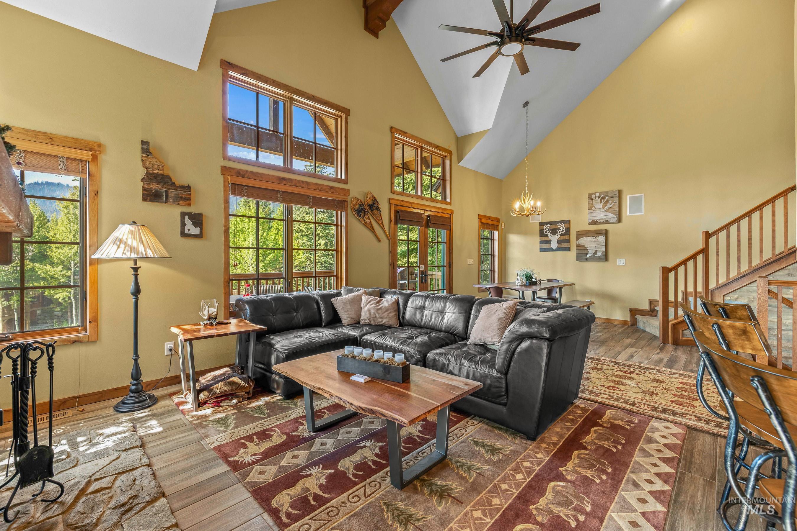 Living room featuring high vaulted ceiling, beamed ceiling, newly finished floors, a chandelier, and stairway