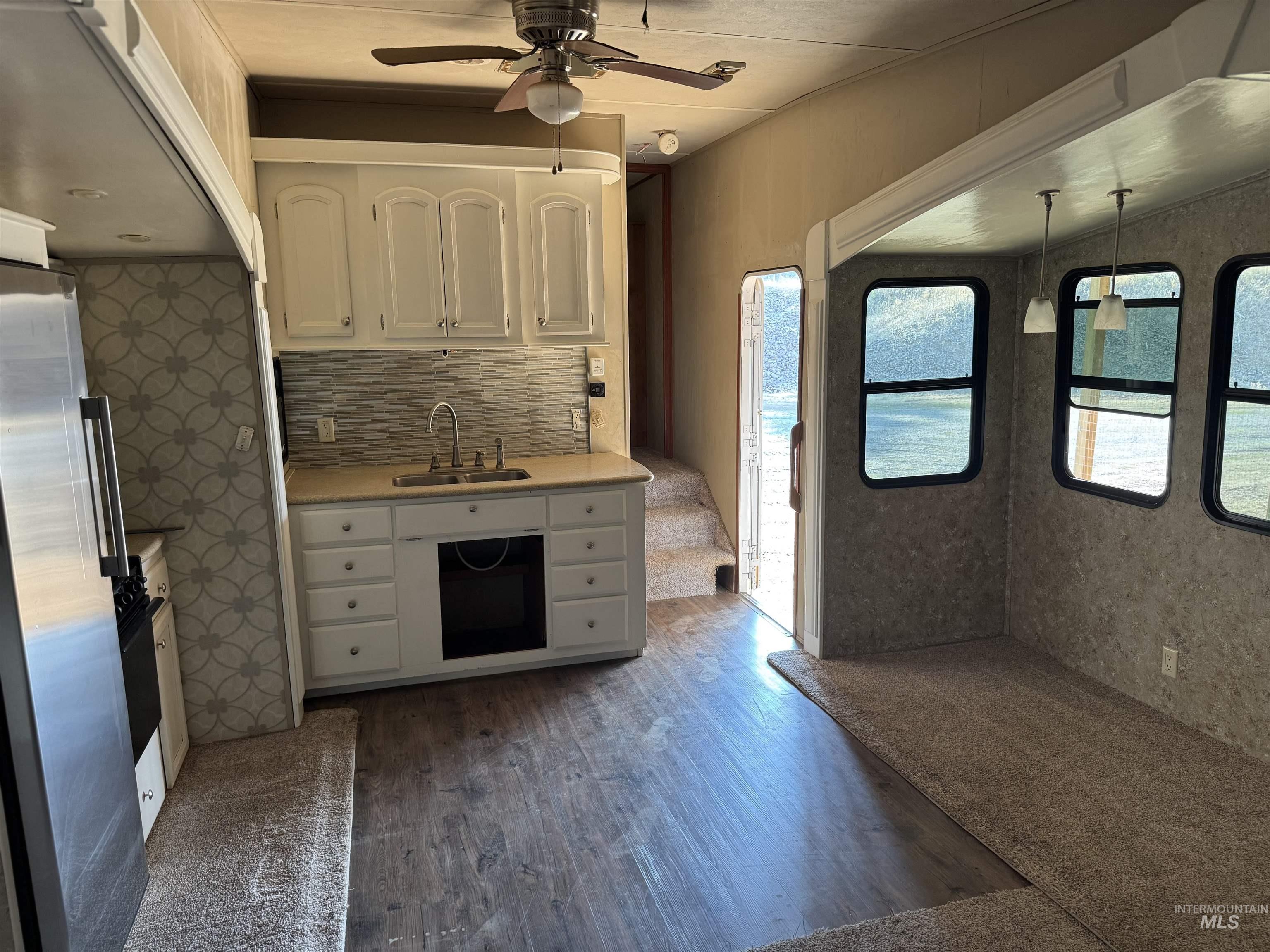 Kitchen with dark wood-style floors, backsplash, freestanding refrigerator, white cabinets, and ceiling fan