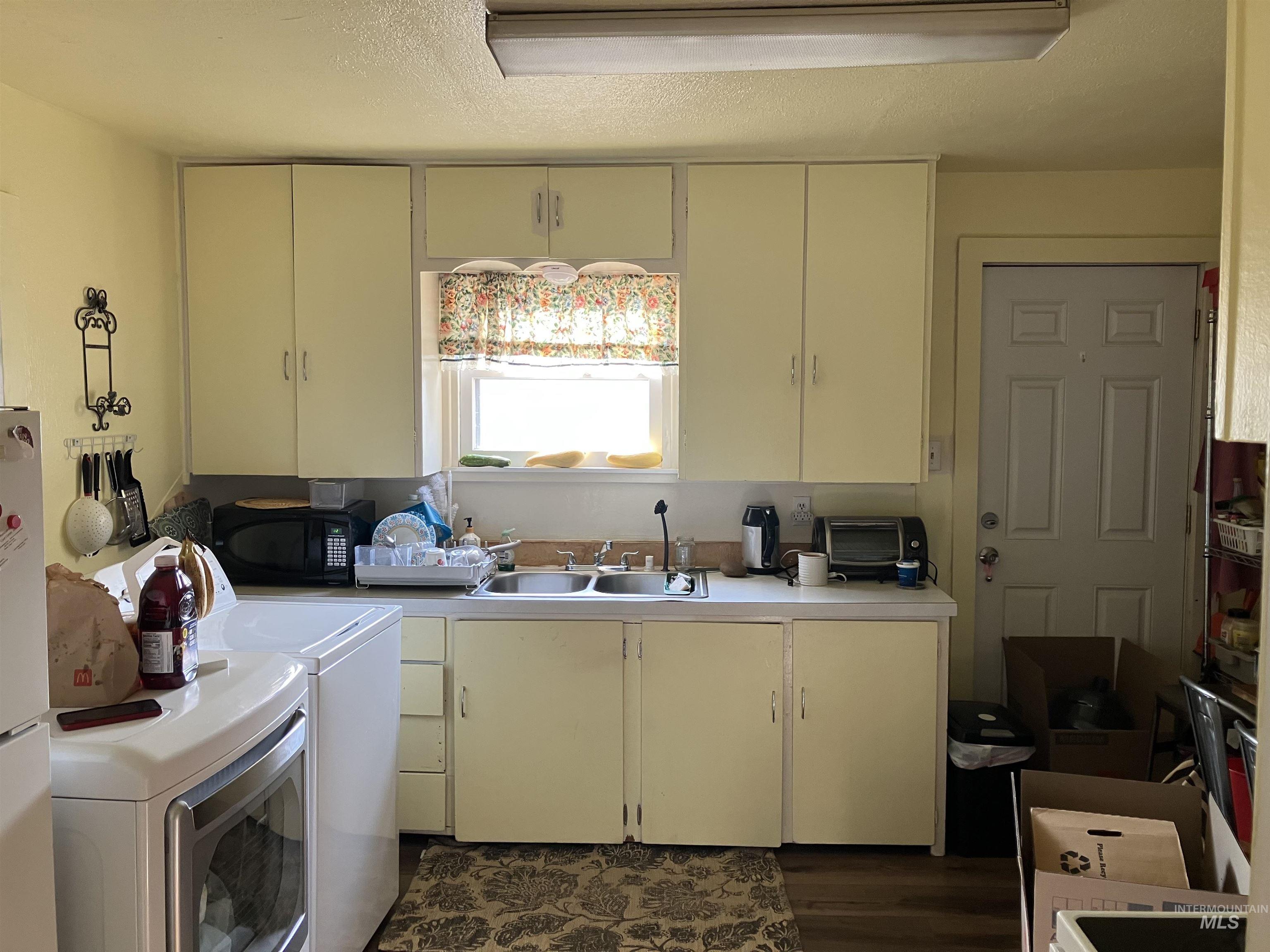 Kitchen featuring cream cabinets, light countertops, a textured ceiling, washer and dryer, and dark wood finished floors