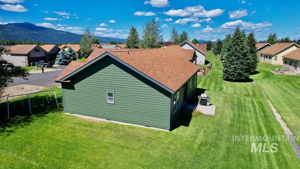 View of side of property with a residential view, a yard, and a shingled roof