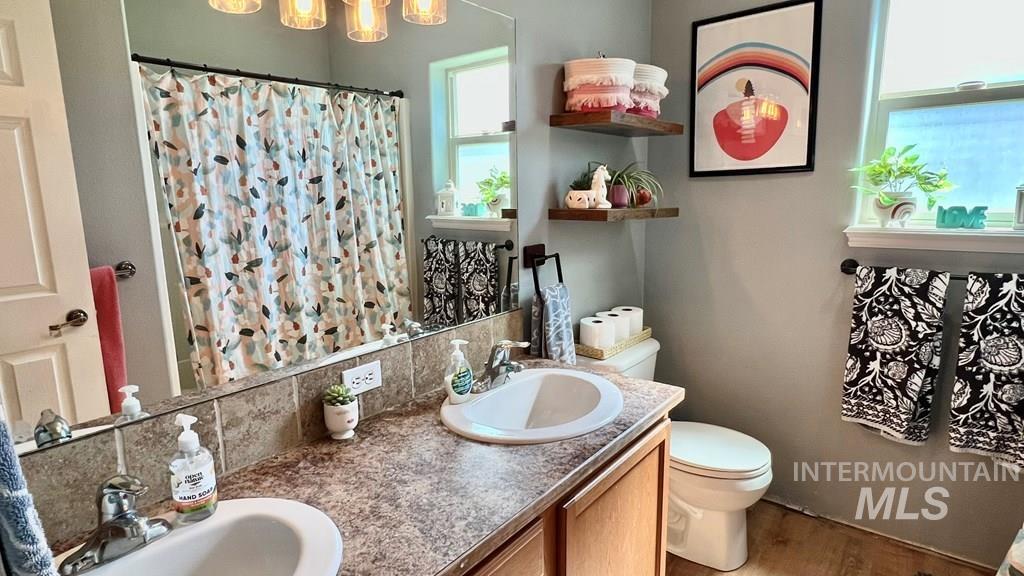 Full bathroom with wood finished floors, double vanity, backsplash, curtained shower, and a chandelier