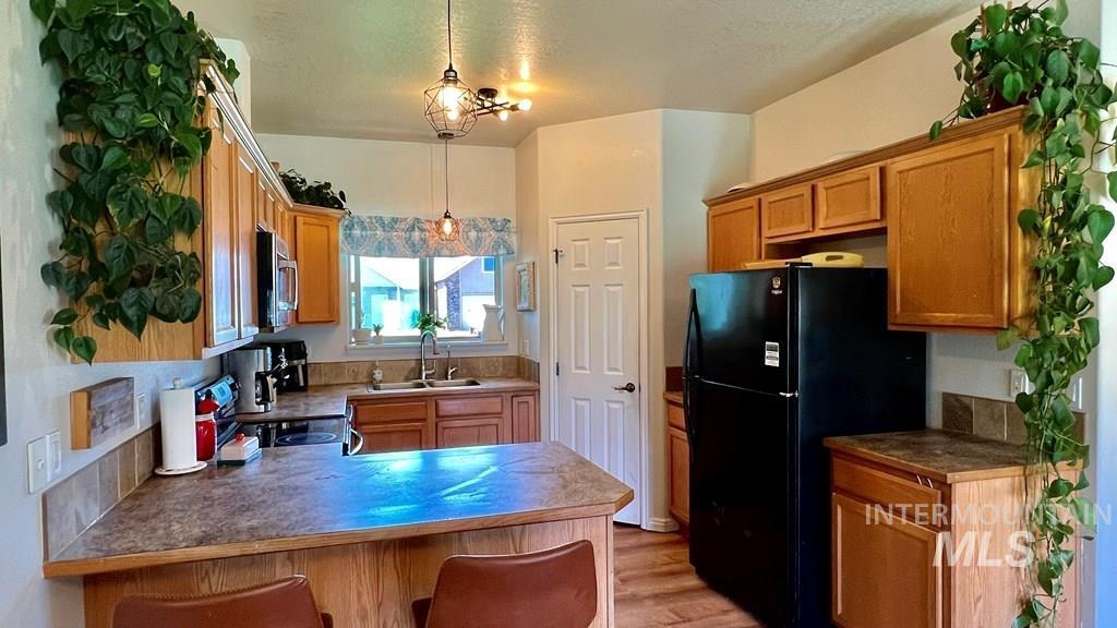 Kitchen with a peninsula, a kitchen bar, freestanding refrigerator, light wood finished floors, and stainless steel microwave