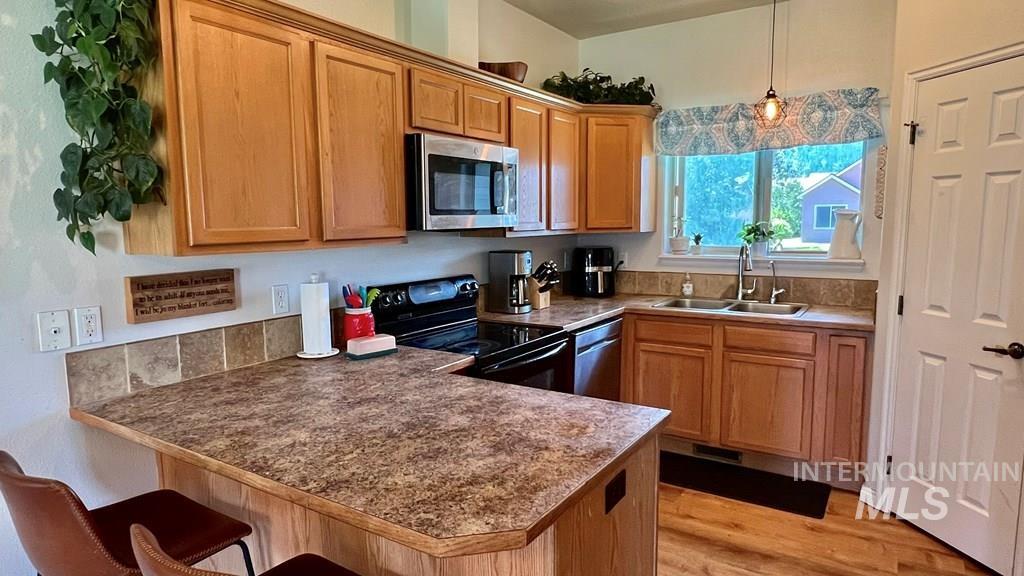 Kitchen featuring a breakfast bar, stainless steel appliances, dark countertops, light wood-type flooring, and pendant lighting