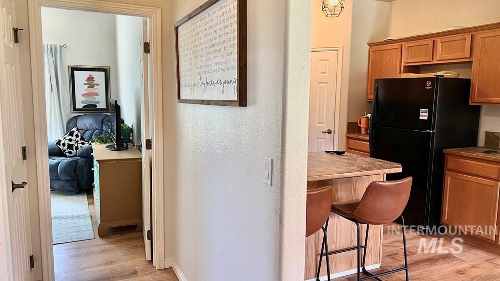 Kitchen with light wood-type flooring, brown cabinets, freestanding refrigerator, a textured wall, and a kitchen breakfast bar