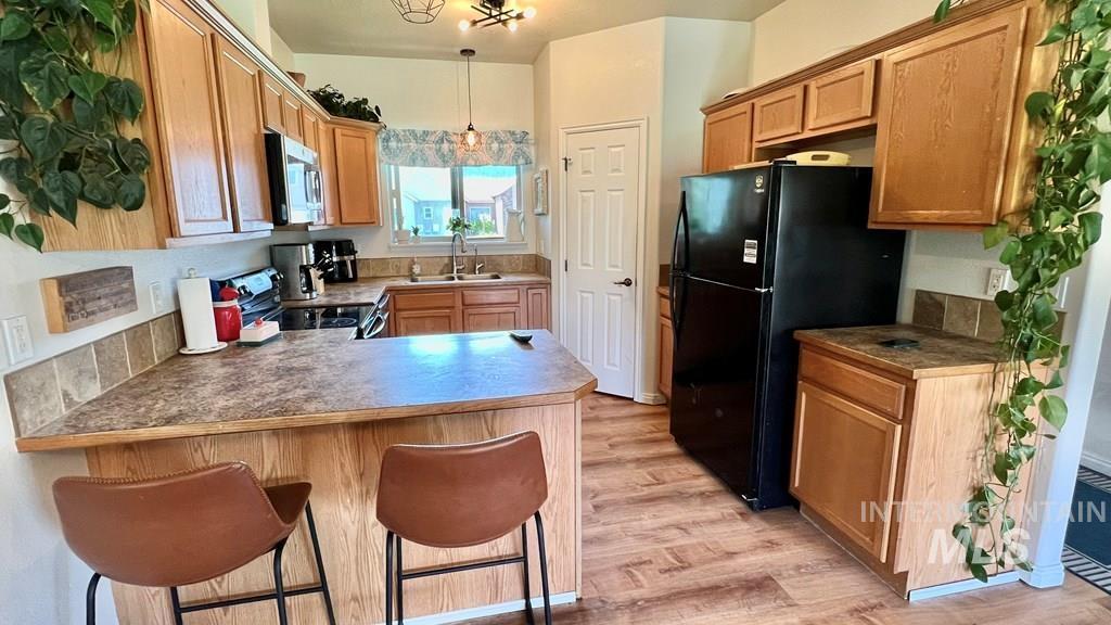Kitchen featuring a breakfast bar, a peninsula, light wood-style flooring, appliances with stainless steel finishes, and dark countertops