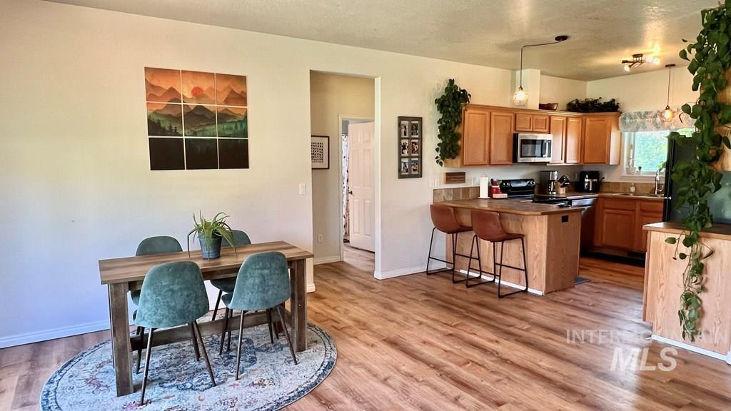 Kitchen with a peninsula, a breakfast bar, black appliances, light wood-style flooring, and pendant lighting