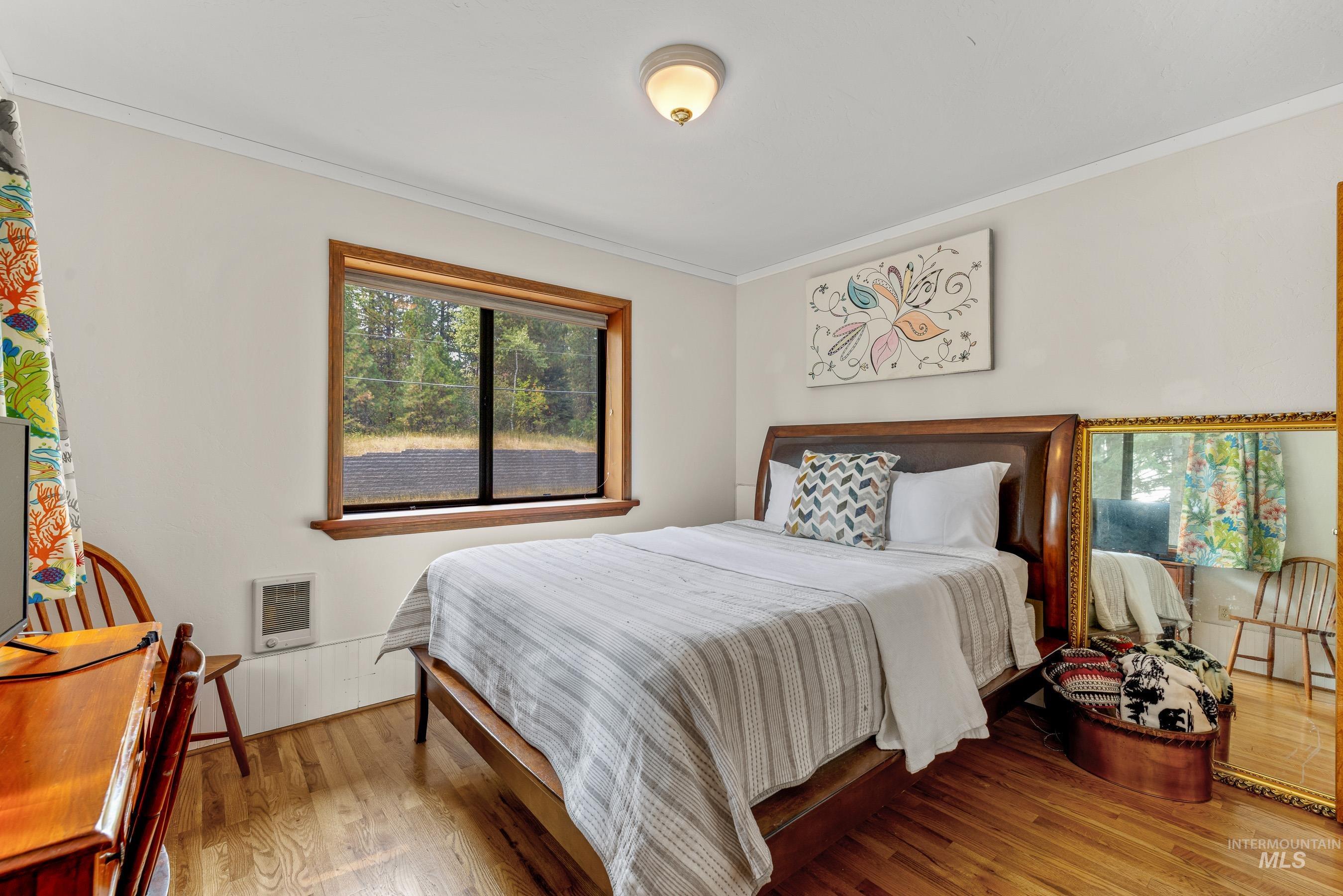 Bedroom featuring ornamental molding, wood finished floors, and heating unit