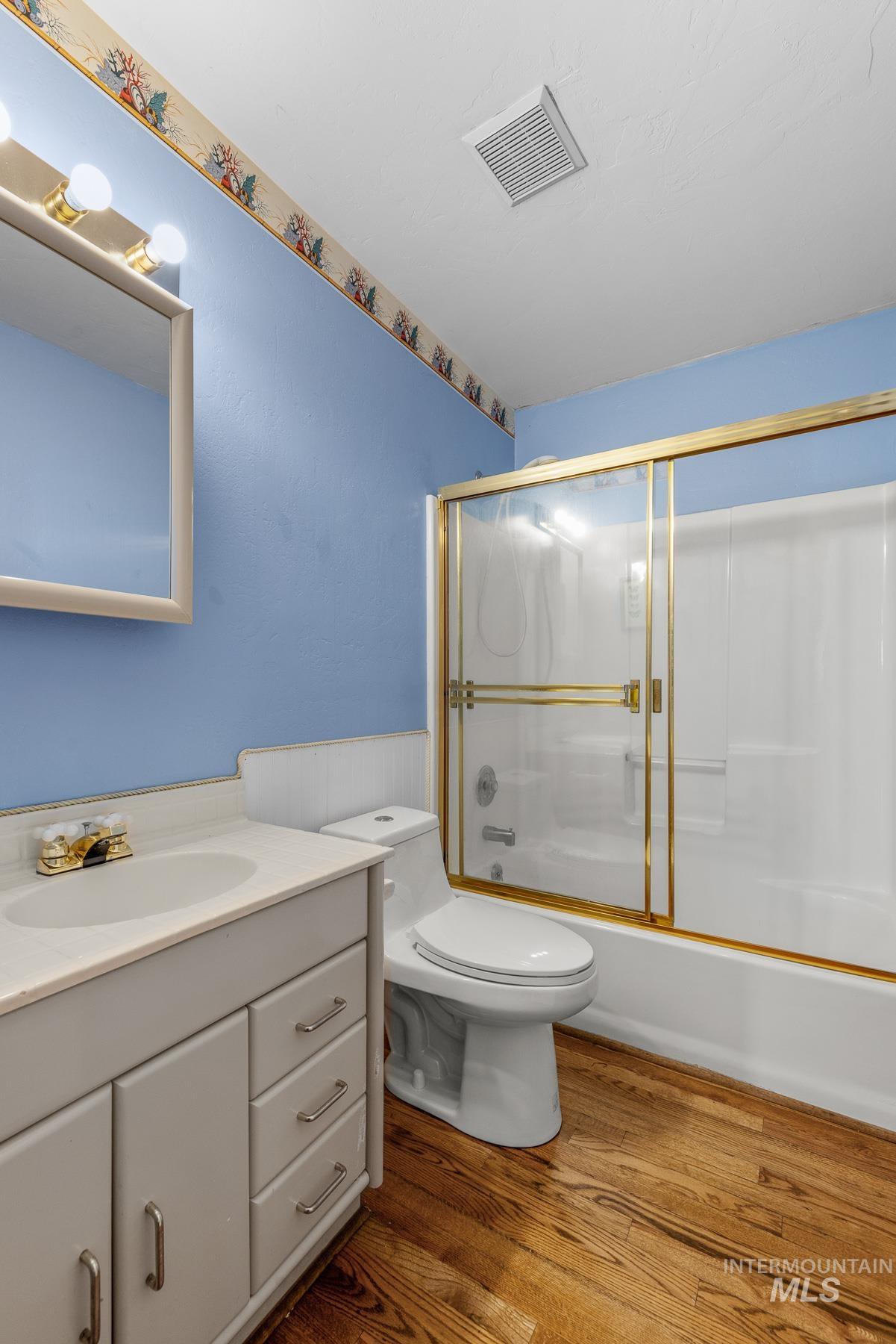 Full bathroom featuring enclosed tub / shower combo, dark wood-style flooring, and vanity