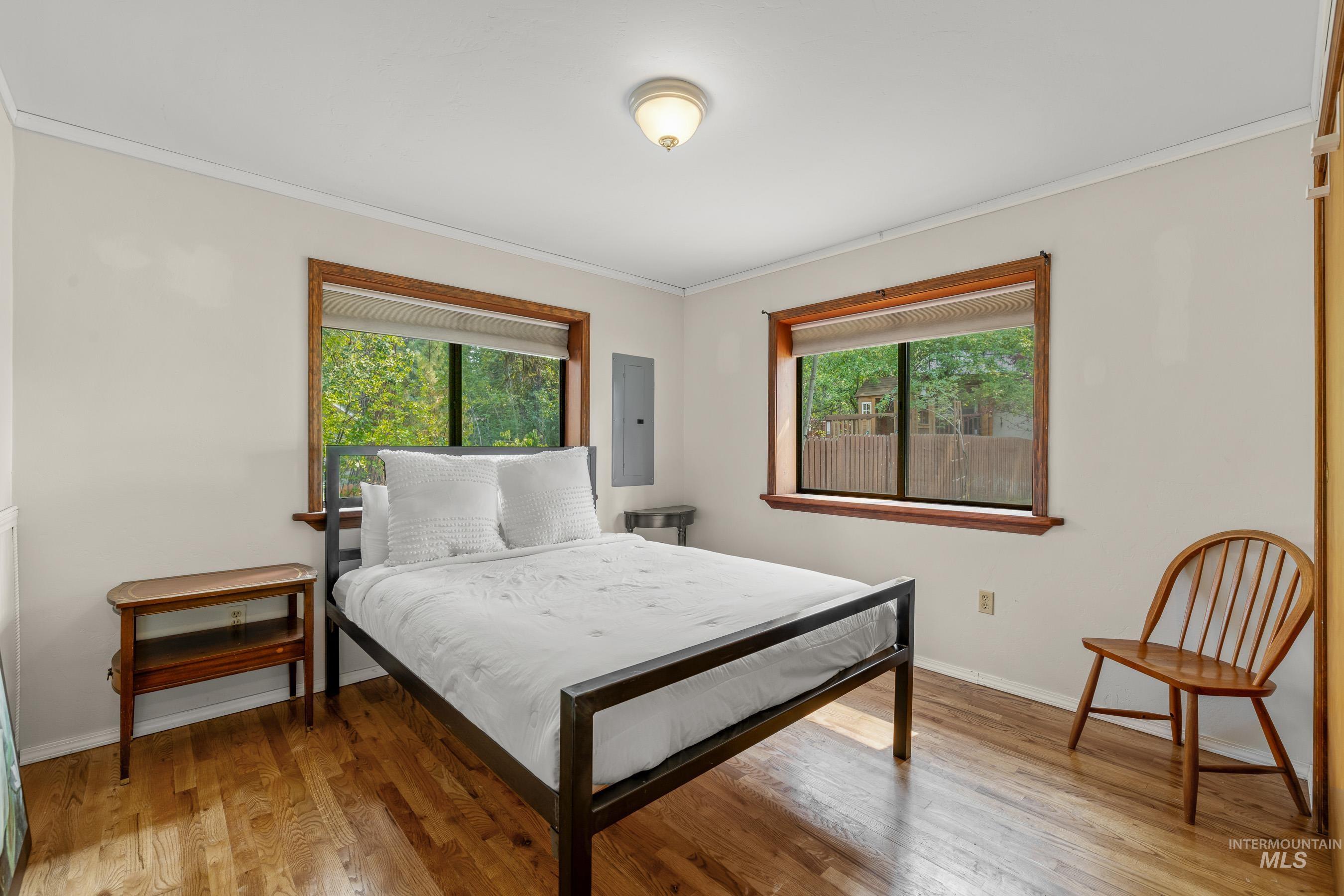 Bedroom featuring multiple windows, light wood-style flooring, crown molding, and electric panel