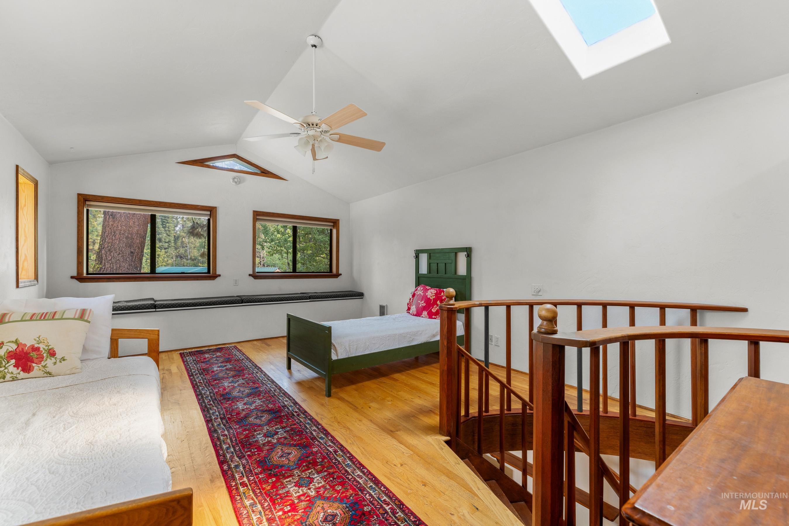 Bedroom featuring a skylight, light wood finished floors, ceiling fan, and high vaulted ceiling