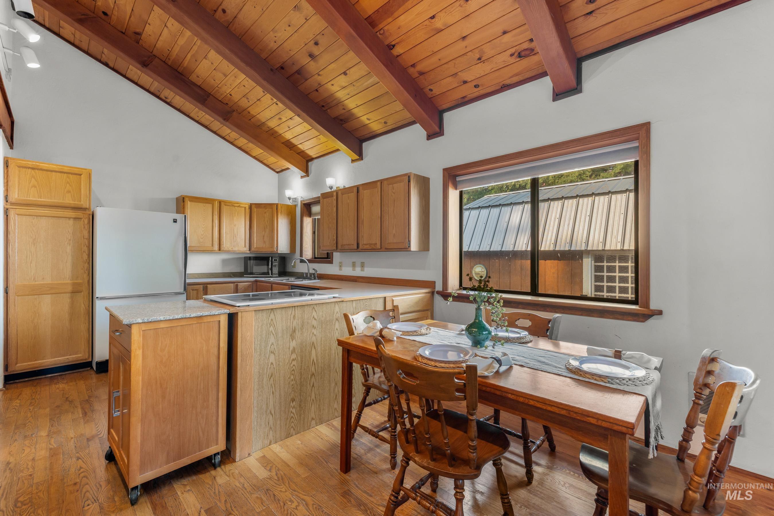 Kitchen with light countertops, light wood-style flooring, white appliances, a wood ceiling with exposed beams, and high vaulted ceiling