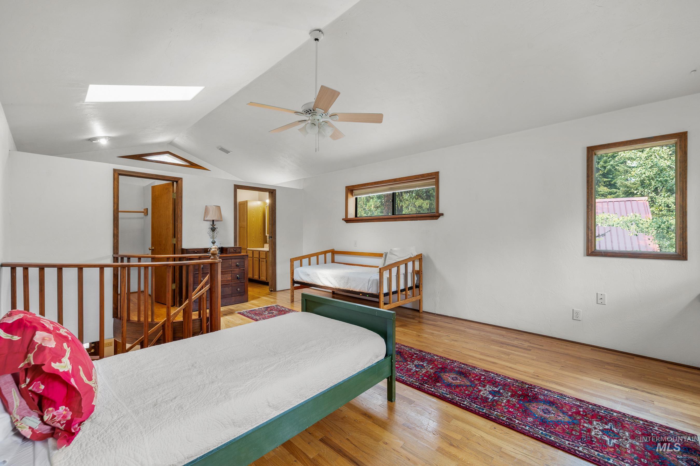 Bedroom featuring vaulted ceiling, light wood finished floors, a skylight, and a ceiling fan