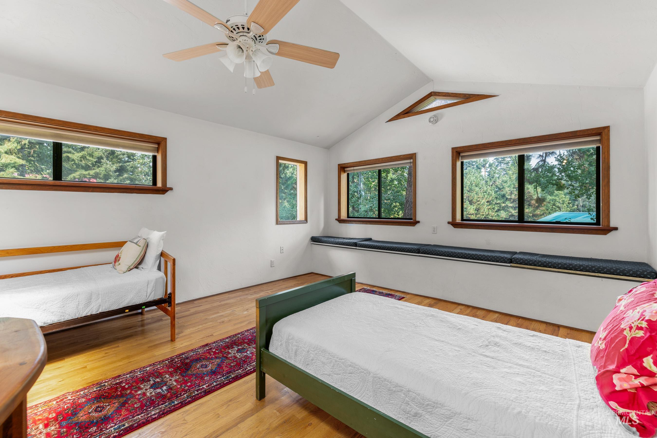 Bedroom with vaulted ceiling, multiple windows, wood finished floors, and ceiling fan