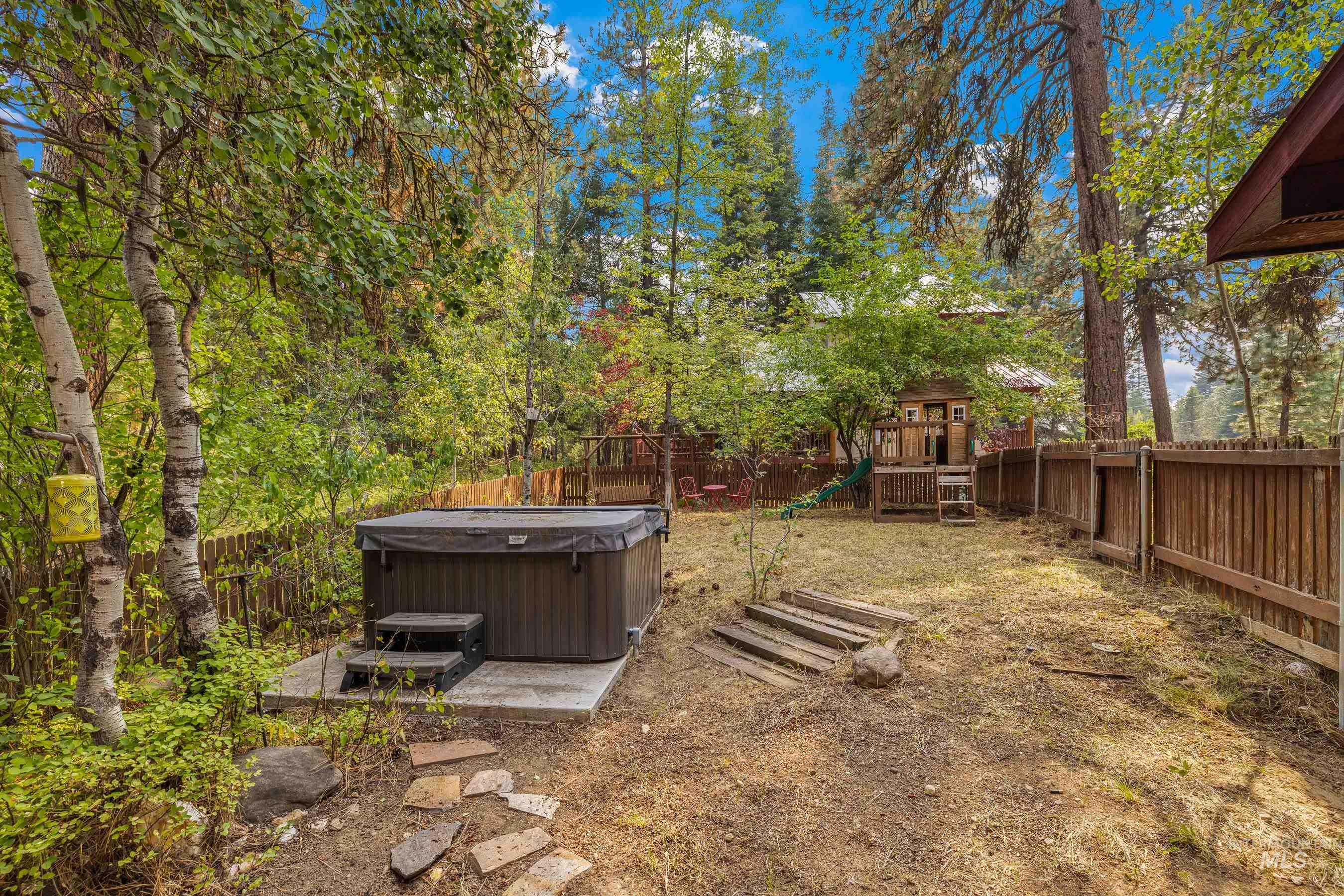 Fenced backyard with a playground and a hot tub