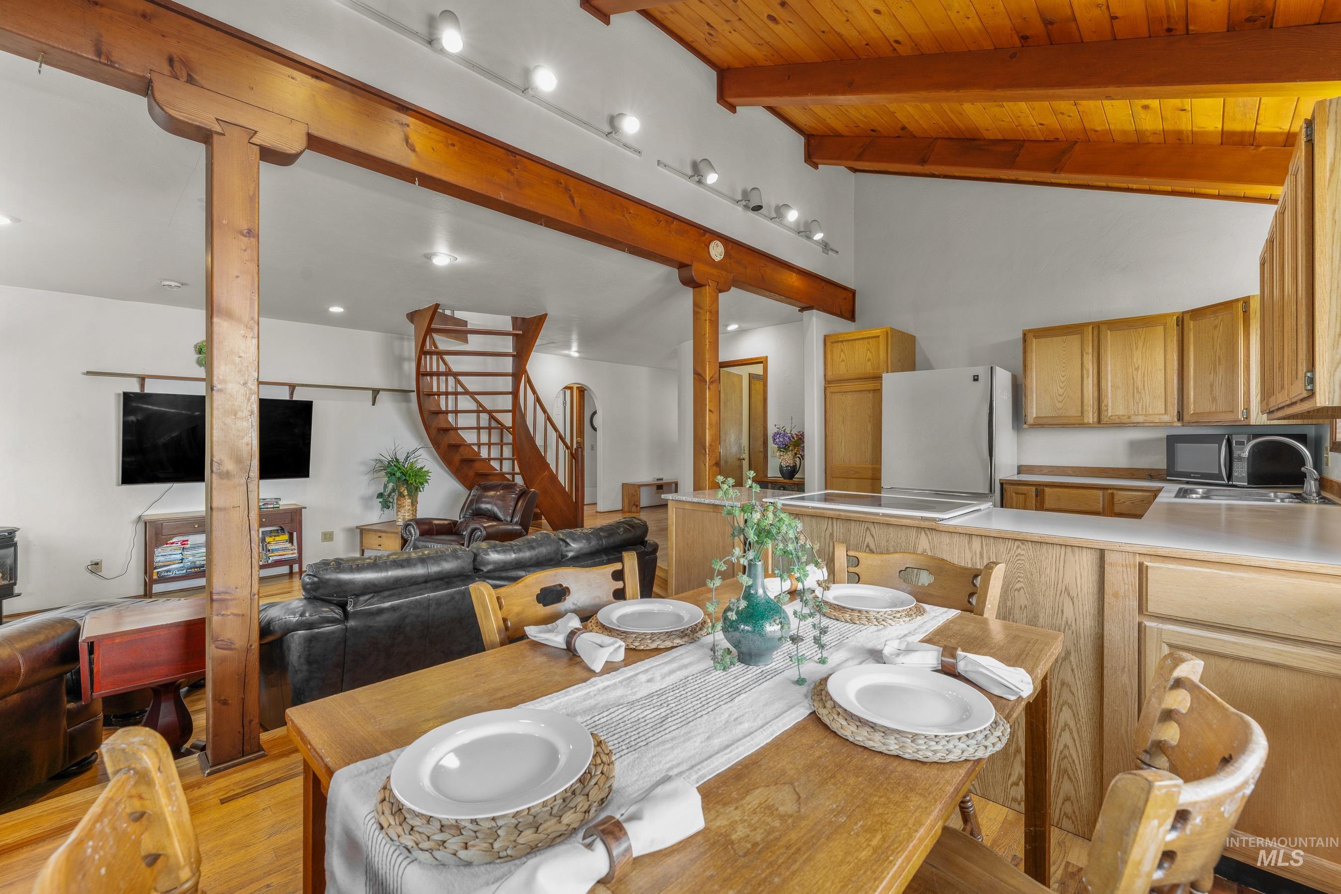 Dining area with light wood-style floors, stairway, high vaulted ceiling, and a wooden ceiling with exposed beams