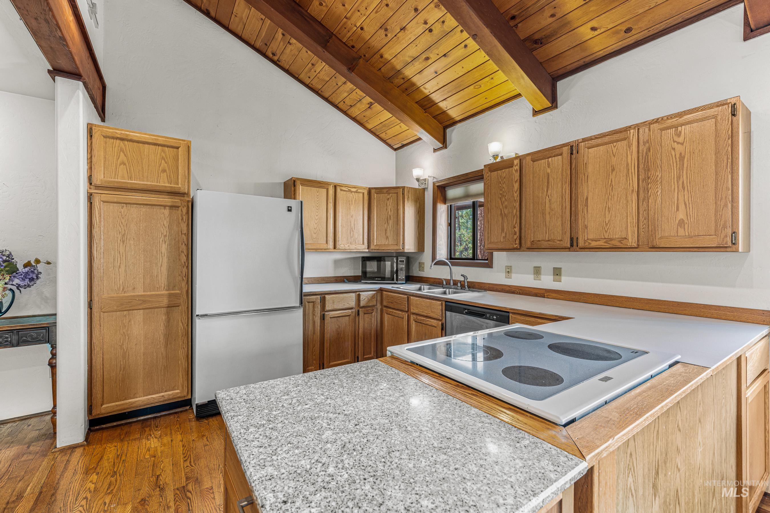 Kitchen with light countertops, freestanding refrigerator, electric cooktop, a wooden ceiling with exposed beams, and high vaulted ceiling