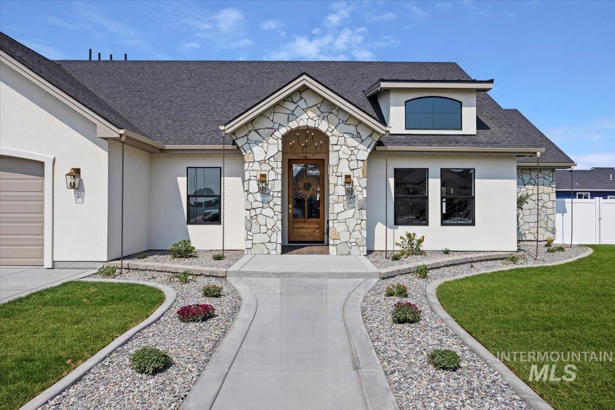 View of front of house with natural stone, beautiful arched entry, thoughtfully designed sidewalk, alder entry door, cedar entry ceiling, chandelier