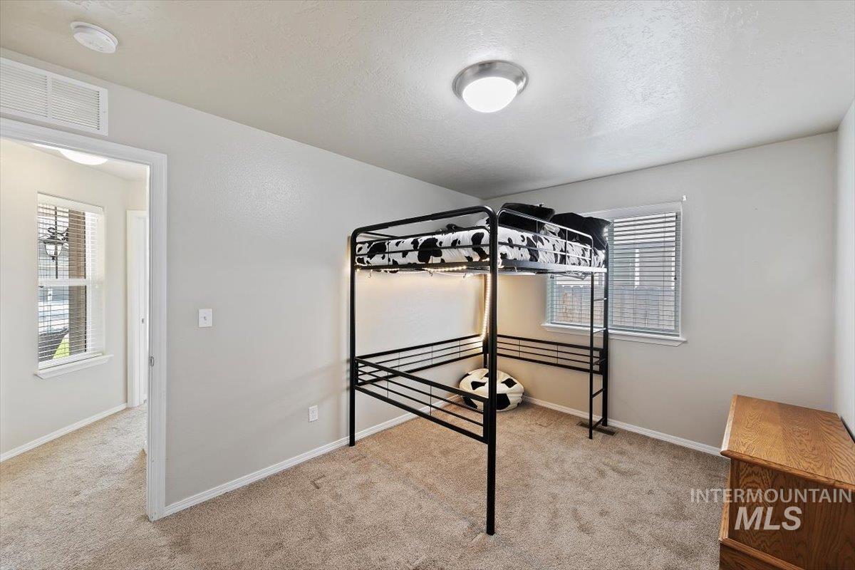 Unfurnished bedroom with light colored carpet, a textured ceiling, and multiple windows
