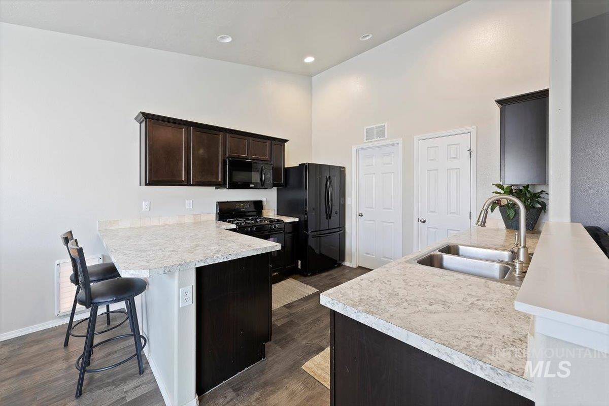Kitchen with a peninsula, light countertops, a breakfast bar area, dark brown cabinets, and black appliances