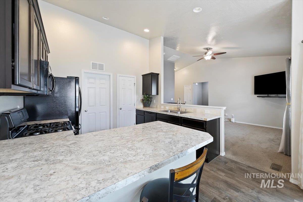 Kitchen with a peninsula, dark wood finished floors, light countertops, a kitchen bar, and high vaulted ceiling