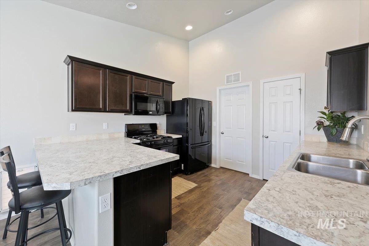 Kitchen with black appliances, dark wood finished floors, light countertops, a kitchen breakfast bar, and dark brown cabinetry