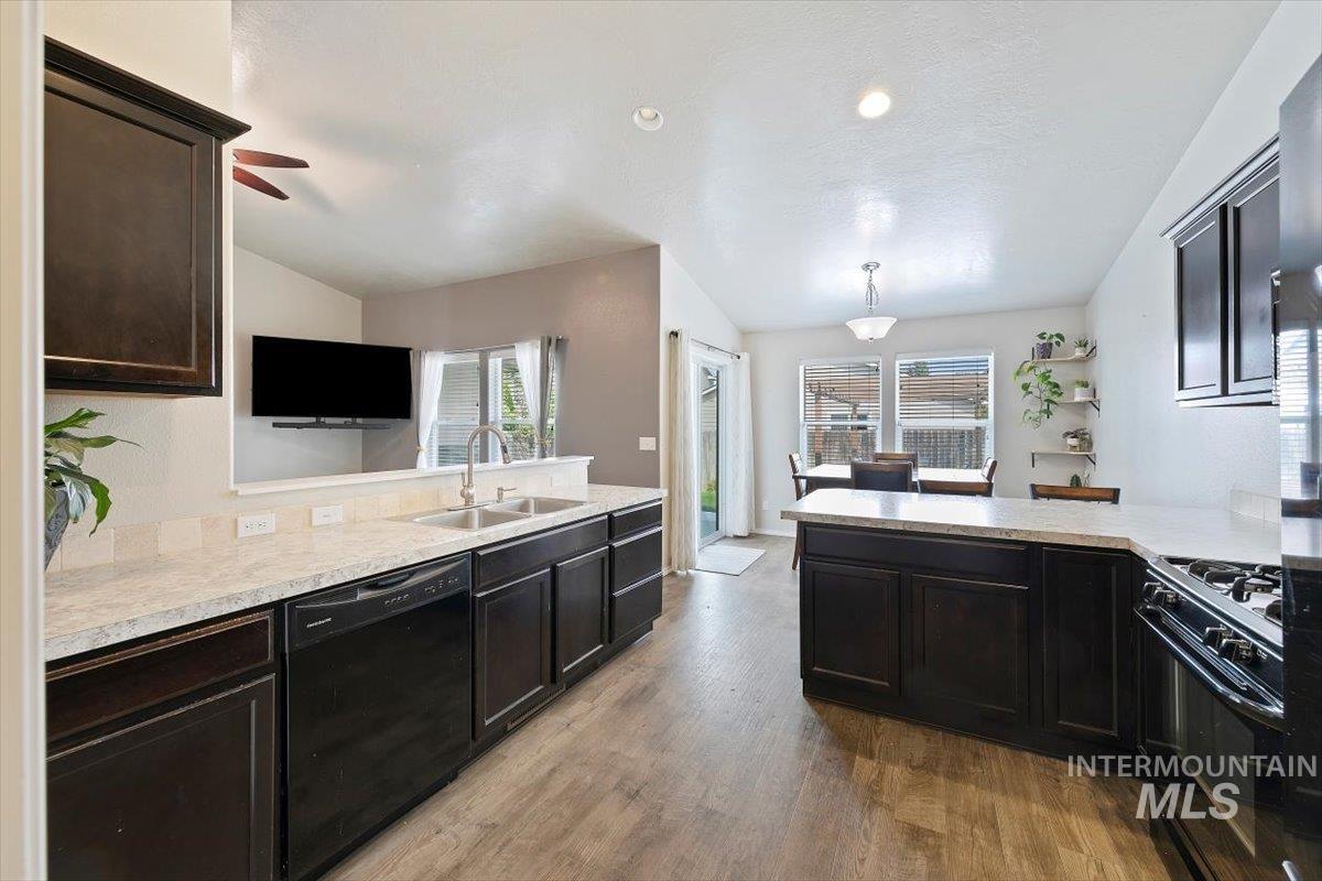 Kitchen featuring a peninsula, black appliances, hanging light fixtures, light wood-style flooring, and ceiling fan