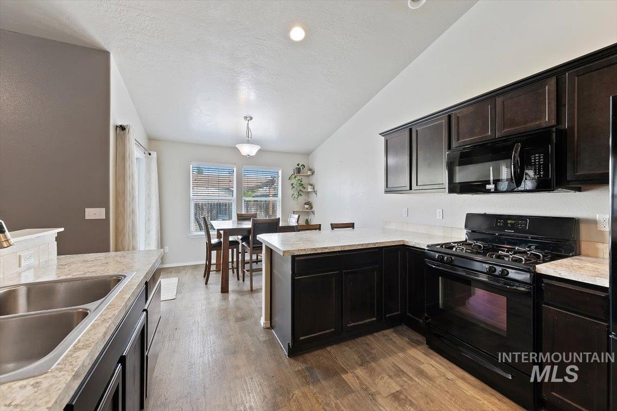 Kitchen with black appliances, a peninsula, dark wood-style flooring, pendant lighting, and a textured ceiling