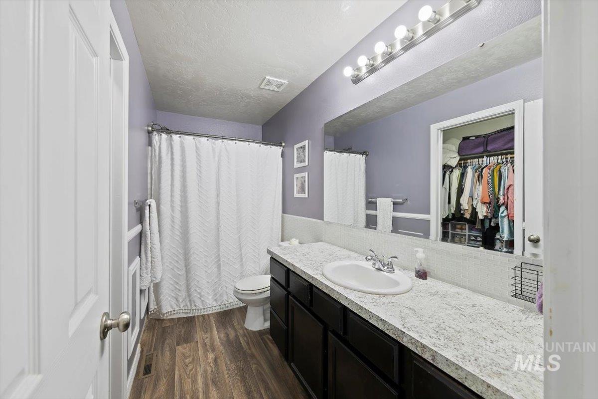Bathroom with dark wood-style floors, vanity, a textured ceiling, a walk in closet, and tasteful backsplash