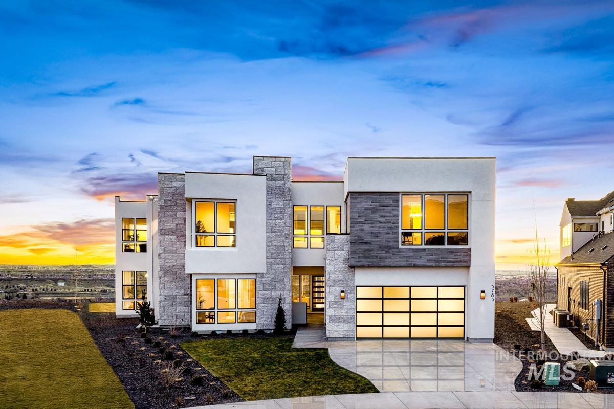 Contemporary house featuring concrete driveway, stone siding, a garage, stucco siding, and a lawn
