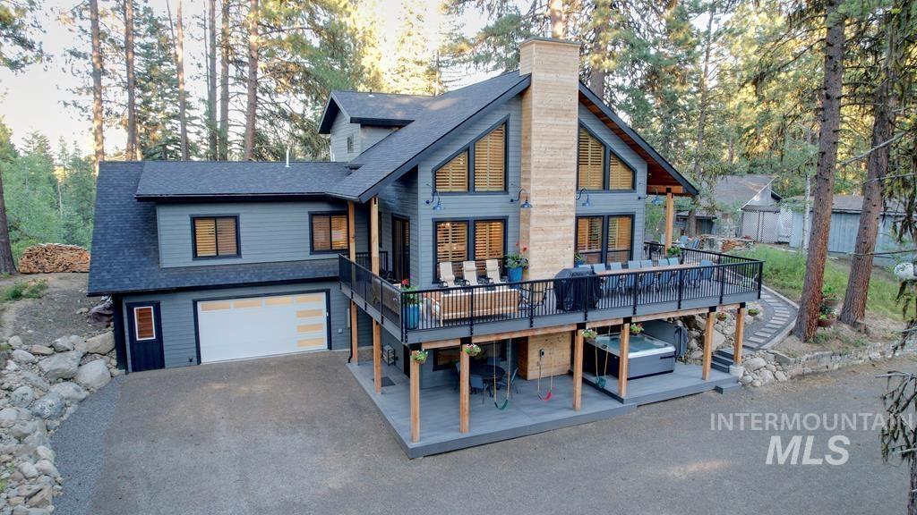 Back of property featuring a shingled roof, a deck, a chimney, and stairs
