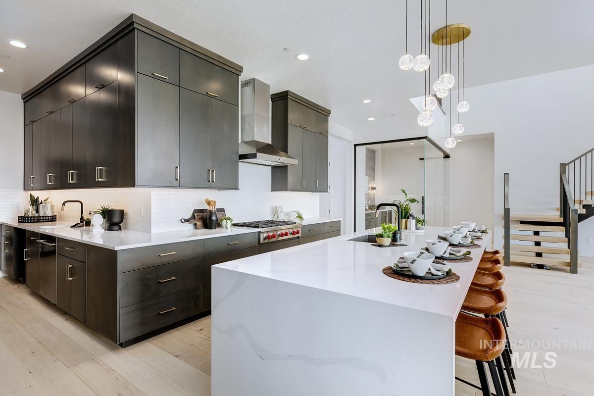 Kitchen with decorative light fixtures, light wood-style flooring, a kitchen breakfast bar, backsplash, and a large island with sink