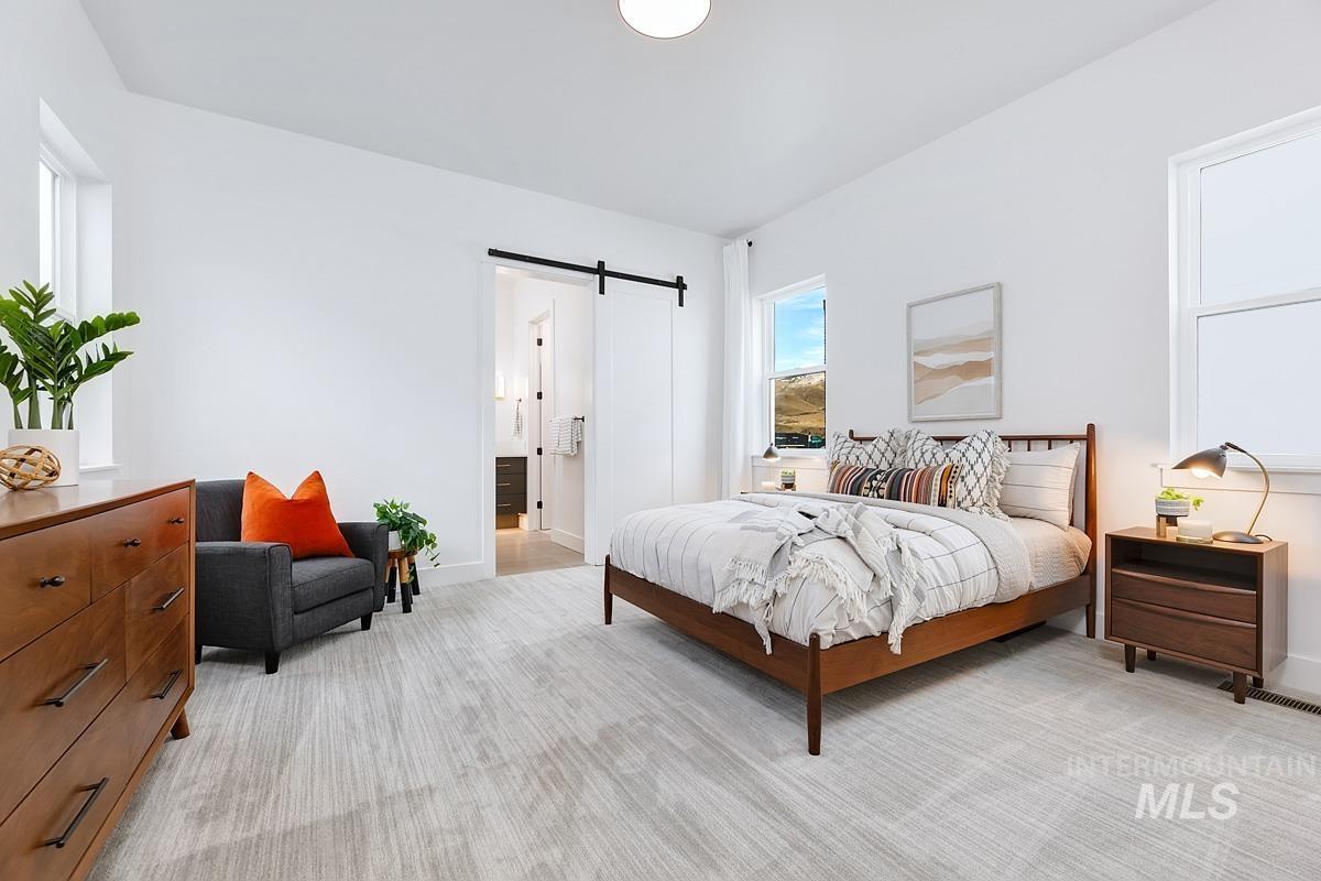 Bedroom with a barn door, light colored carpet, and ensuite bath