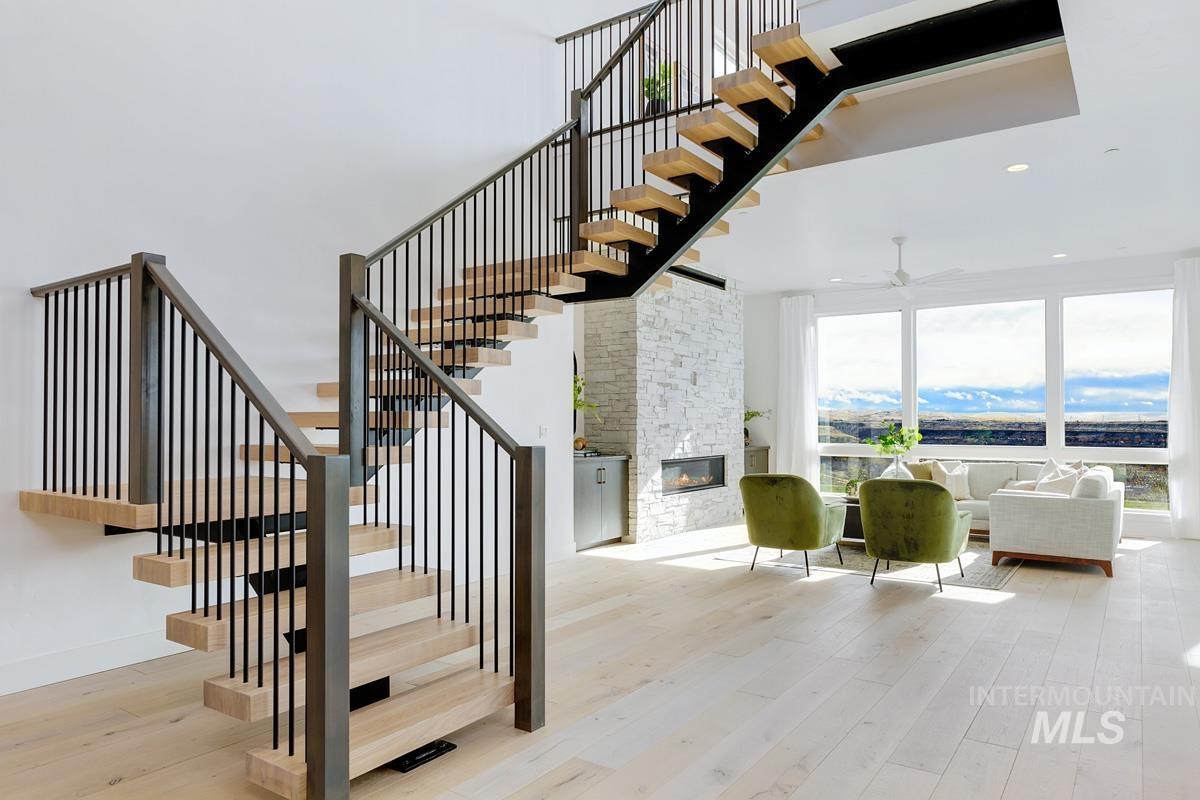 Staircase with hardwood / wood-style floors, a stone fireplace, ceiling fan, recessed lighting, and a towering ceiling