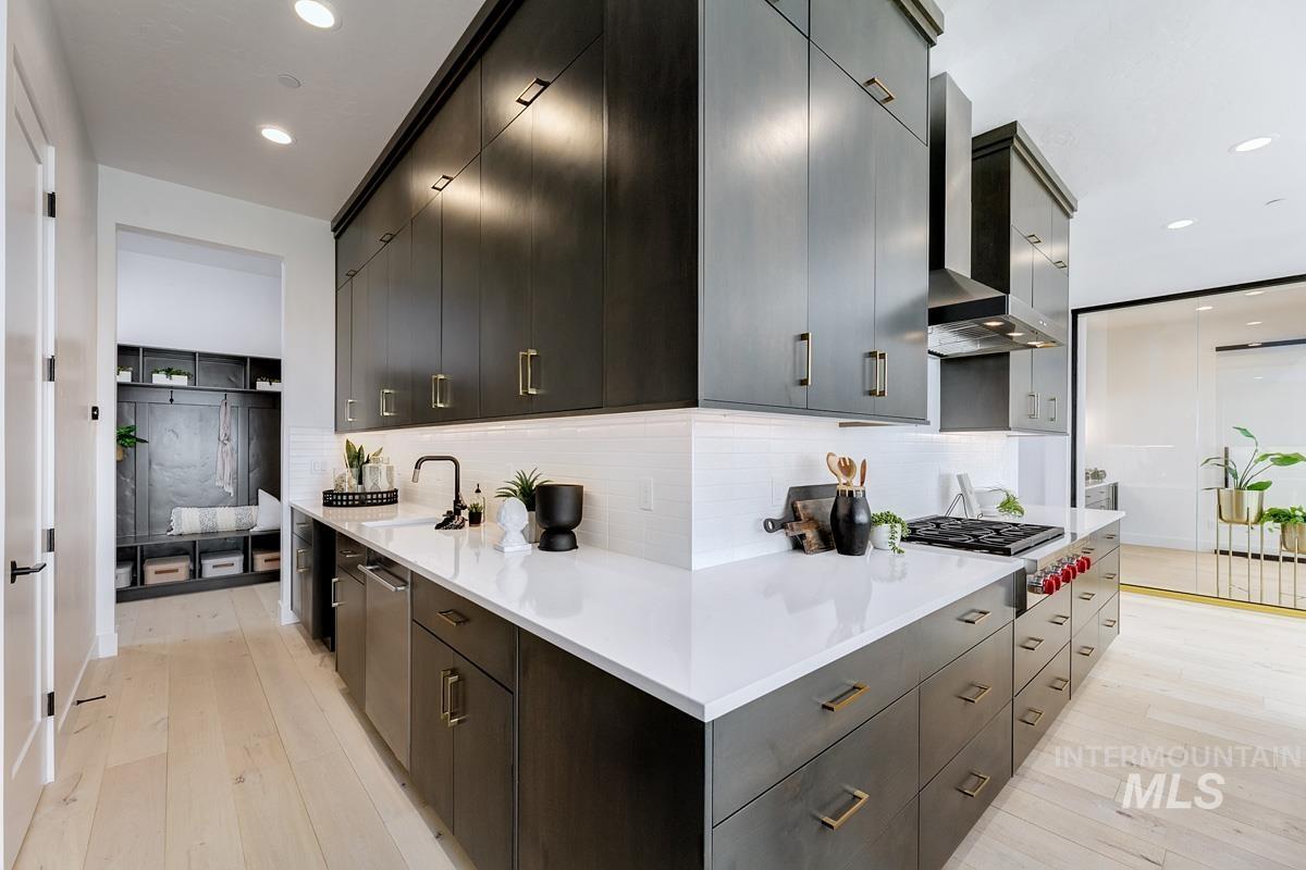 Kitchen with backsplash, light wood-style flooring, recessed lighting, wall chimney exhaust hood, and appliances with stainless steel finishes