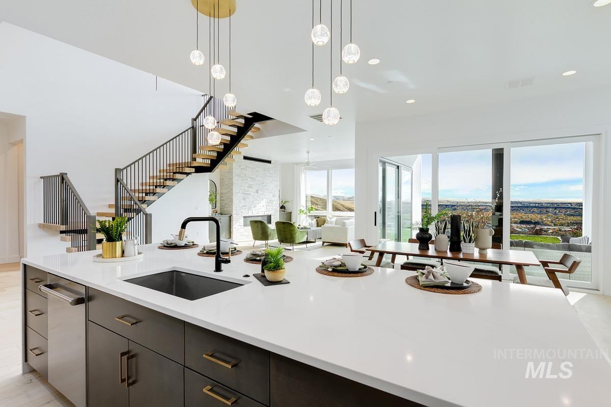 Kitchen with hanging light fixtures, light stone countertops, open floor plan, an island with sink, and stainless steel dishwasher