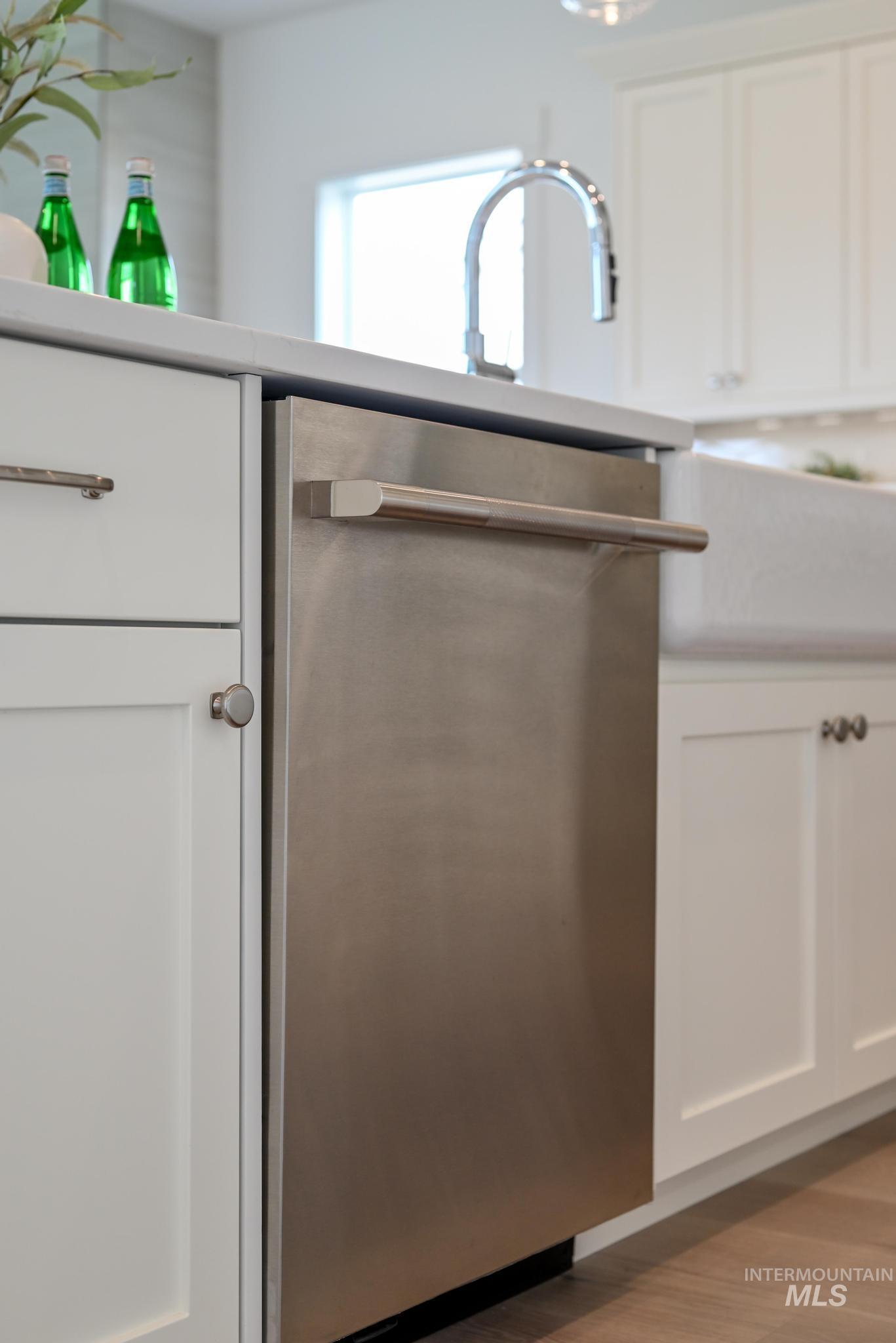 Kitchen view of dishwasher, white cabinets, and light wood-style floors