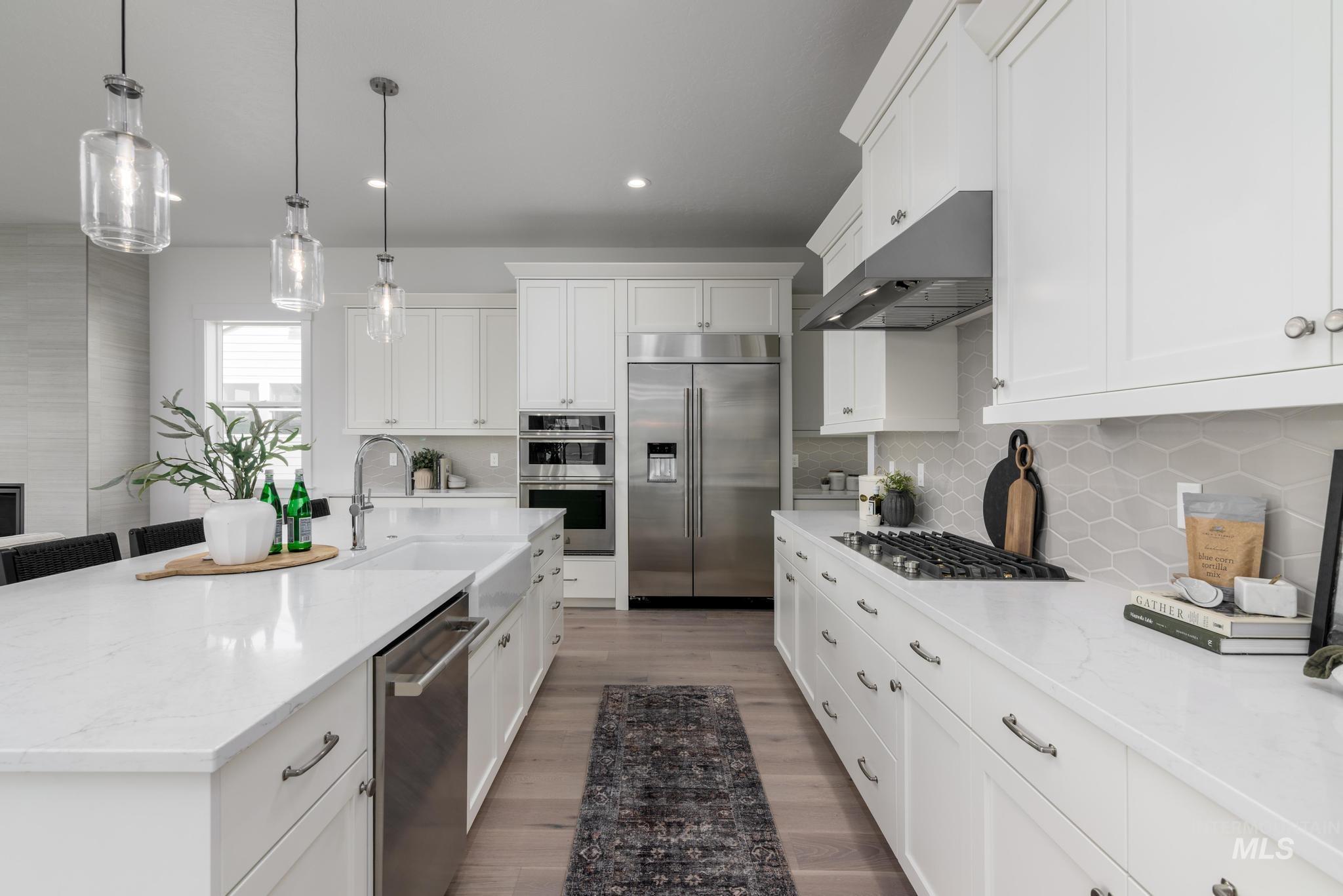 Kitchen with light stone countertops, pendant lighting, stainless steel appliances, a center island with sink, and white cabinetry