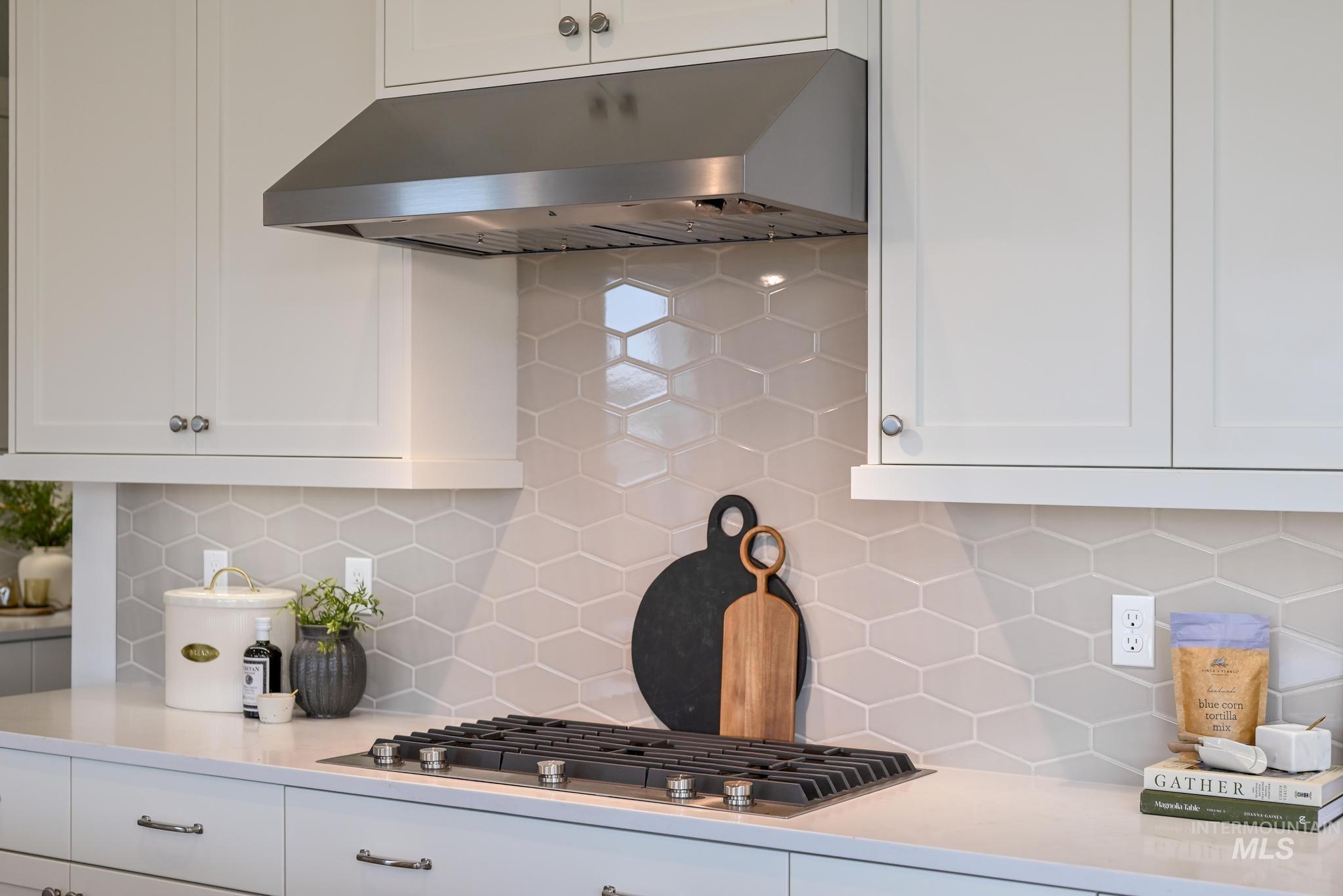 Kitchen featuring white cabinets, under cabinet range hood, backsplash, stainless steel gas stovetop, and light stone countertops